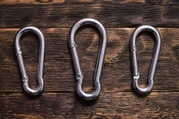 Silver carabiners on a brown wooden board background. - Zdjęcie, obraz