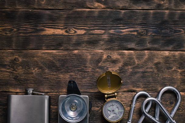 Compass, carabiner, flashlight and water flask on the brown wooden board background with copy space. Travel or adventure. - 写真・画像