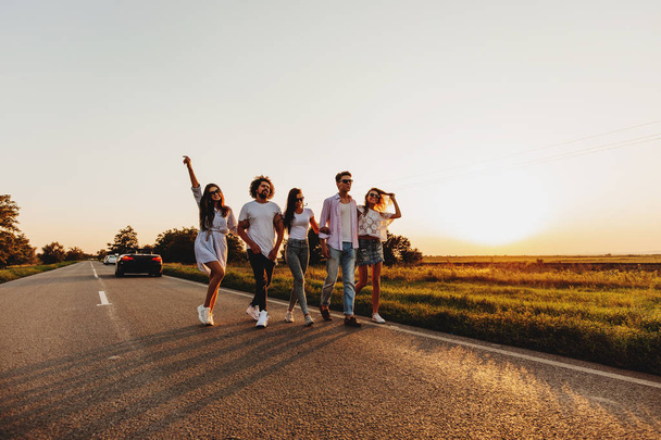 Young stylish two guys and three girls walk on a country road on a sunny day - Foto, Imagem