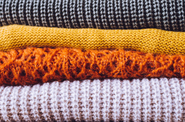 木製のテーブルの上にニットウールセーターの秋の色の山。異なる編みパターンを持つ服は、スタックに折り畳まれています。暖かい居心地の良い冬の秋のニットウェアのコンセプト。スペースのコピー. - 写真・画像