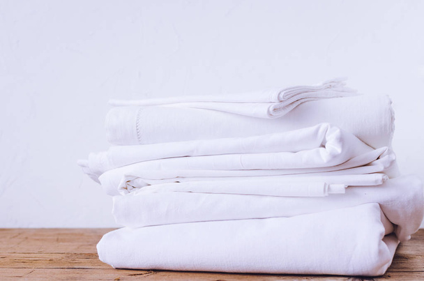 Stack of white linens on table indoor. Household concept. Fresh folded bed sheets. Ironing, laundry, housework concept - close up of pile of linens on table at home. - Photo, Image