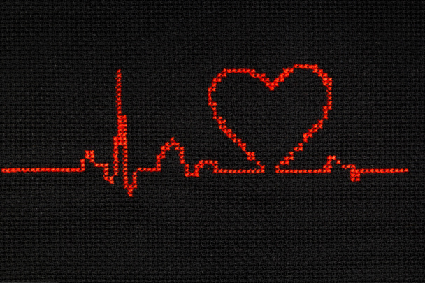 Cardiogram with a heart symbol is embroidered with red thread on a black cloth. - Photo, Image
