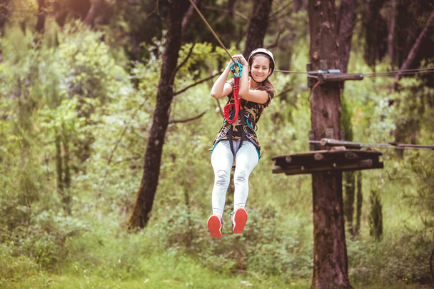 Ευτυχισμένο κορίτσι του σχολείου απολαμβάνοντας τη δραστηριότητα σε ένα πάρκο περιπέτειας αναρρίχηση σε μια καλοκαιρινή μέρα - Φωτογραφία, εικόνα