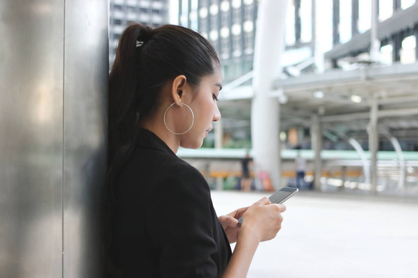Side näkymä houkutteleva nuori aasialainen nainen tilalla mobiili älypuhelin kadulla kaupungin. Sosiaalisen verkoston käsite
 - Valokuva, kuva