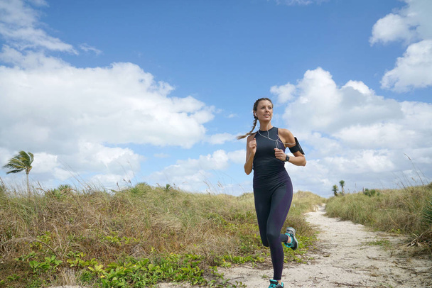 Athletic young woman running on beachy landscape - Foto, Imagen