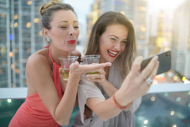 Due bellissimi amici scattano selfie sul bar sul tetto con luci della città sullo sfondo
 - Foto, immagini