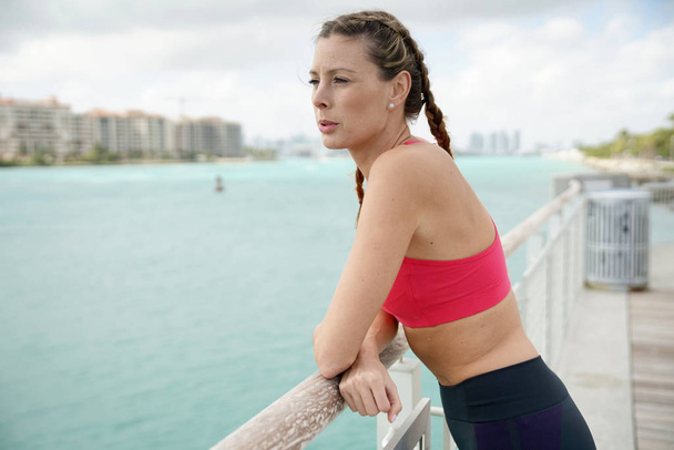 Attractive woman in sportswear thinking by waterfront after run - Foto, Imagem