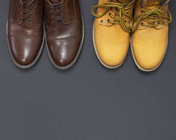 Zapatos para hombre clásicos de cuero marrón y botas de trabajo amarillas para hombre de nobuck natural sobre fondo negro gris vista superior plano laico espacio de copia. Concepto masculino de moda, zapatos de cuero genuino, venta, tienda
 - Foto, Imagen