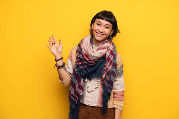 Mutlu ifade ile el ile sarı duvar selamlayan üzerinde genç hippi kadın - Fotoğraf, Görsel