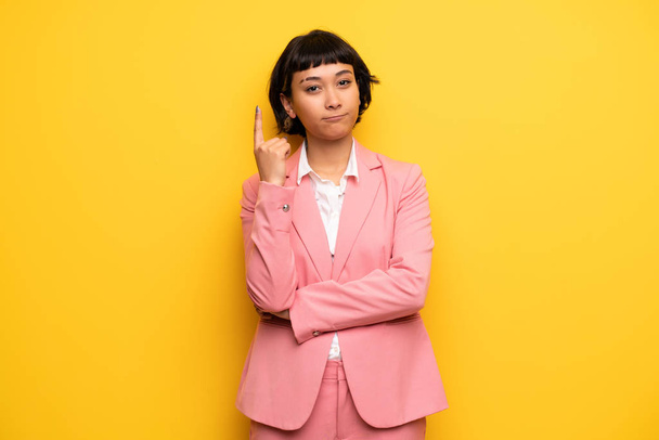 Современная женщина в розовом деловом костюме думает об идее, показывая пальцем вверх
 - Фото, изображение