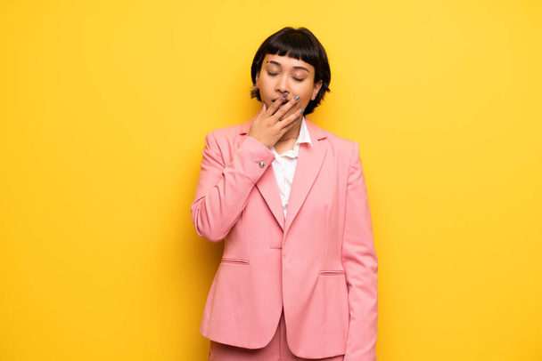 Современная женщина в розовом деловом костюме зевает и закрывает широко раскрытый рот рукой
 - Фото, изображение