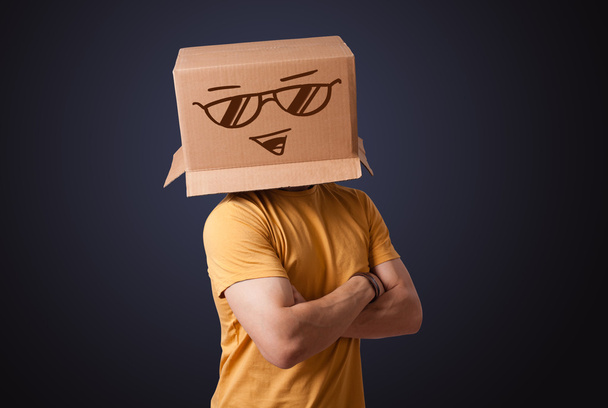 Young man gesturing with a cardboard box on his head with smiley - Фото, изображение