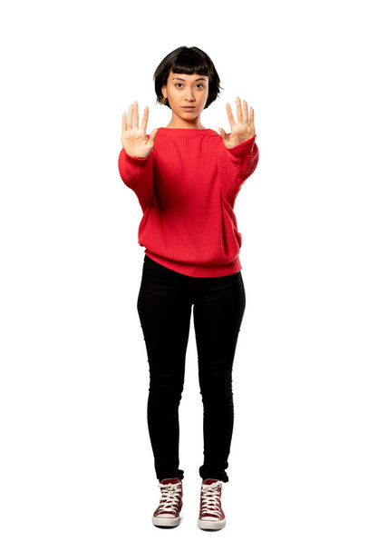 A full-length shot of a Short hair girl with red sweater making stop gesture and disappointed over isolated white background - Фото, изображение