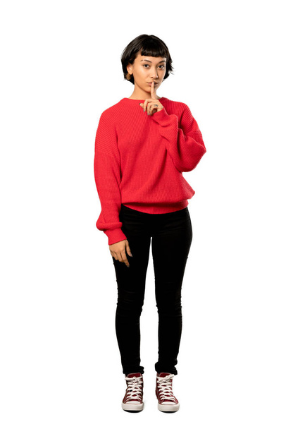 A full-length shot of a Short hair girl with red sweater showing a sign of silence gesture putting finger in mouth over isolated white background - Photo, image