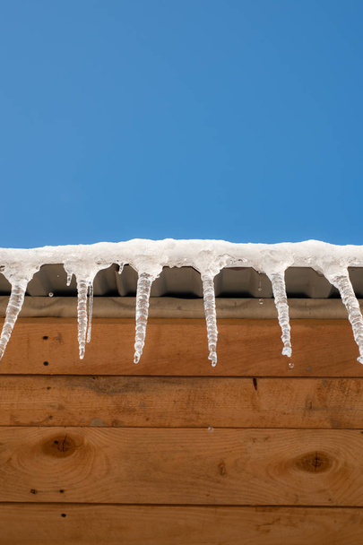 ワイナー天気。つらら。凍結する冬アイコン背景。家の屋根から垂れ下がっているつらら。氷のクローズ アップ。建物は、大きな氷柱で覆われて。危険な氷。もうすぐ春です。. - 写真・画像