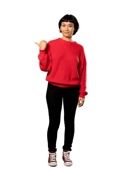 Una foto completa de una chica de pelo corto con suéter rojo apuntando hacia un lado para presentar un producto sobre un fondo blanco aislado
 - Foto, imagen