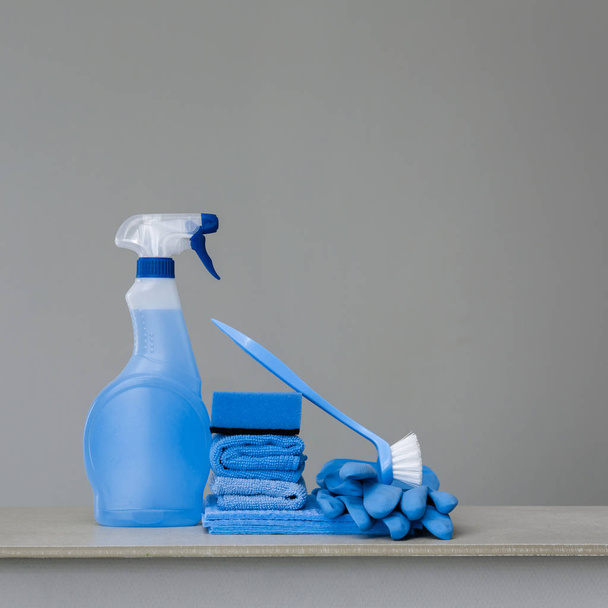 Limpiar el atomizador azul con dispensador de plástico, esponja, limpieza cepillo para plato, paño para el polvo y guantes de goma en fondo gris. Equipos de limpieza. Copia espacio. - Foto, imagen