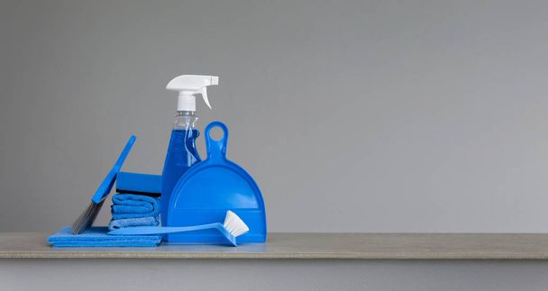 Blue cleaning kit on neutral background: Spray detergent, dishwashing brush, dust cloths, sponge, scoop and broom. Copy space. - 写真・画像