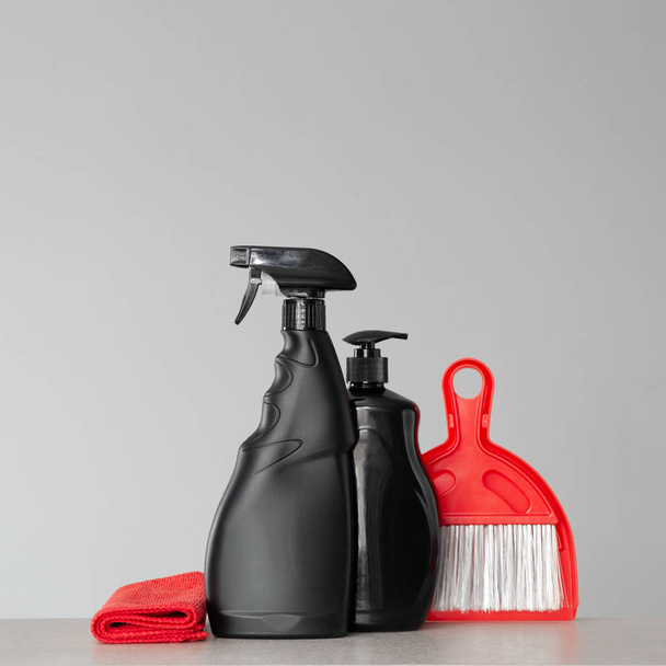Black cleaning products and red cleaning tools on neutral background. Copy space. - Fotografie, Obrázek