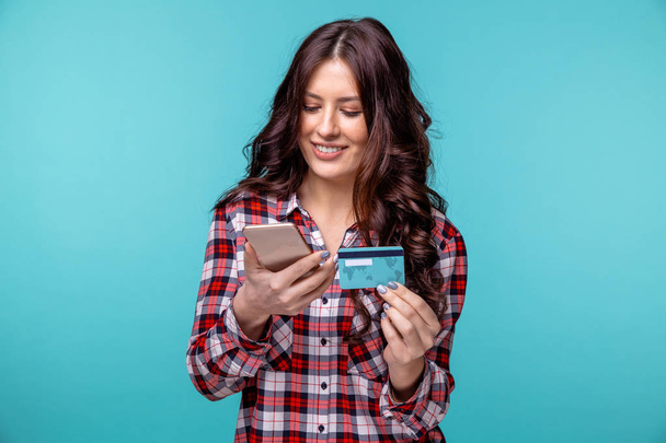 Panienka na białym tle nad niebieskim tle przy użyciu telefonu komórkowego z posiadania karty kredytowej. - Zdjęcie, obraz
