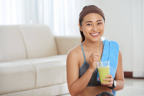 Portrait of young beautiful Asian woman in active wear holding homemade  protein shake and smiling at camera happily - Zdjęcie, obraz