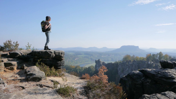 若い女性の旅行者のバックパックを山の崖上に立つ - 映像、動画