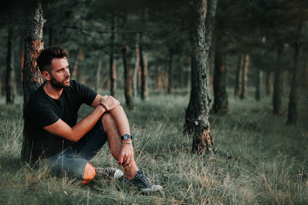 Młody człowiek siedzi na trawie w lesie kontemplując - Zdjęcie, obraz