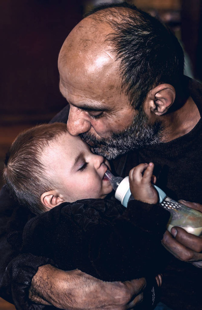 A man kisses a small child and feeds him in his arms - Photo, Image