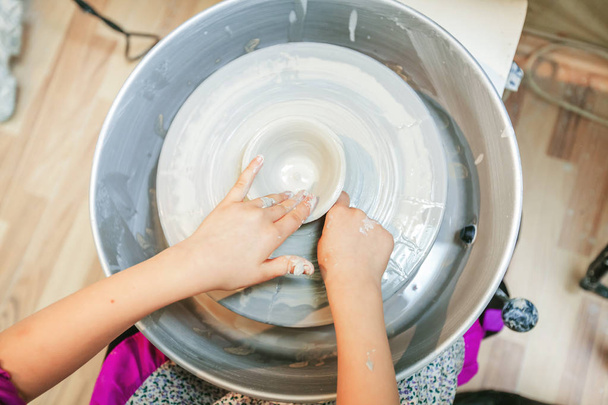 Pohled shora rukou dítě pracovat s hlínou na hrnčířského kruhu. - Fotografie, Obrázek