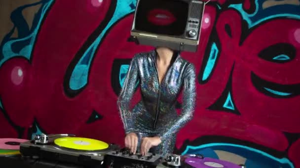 Sexy woman with tv on head djing against graffiti - Footage, Video