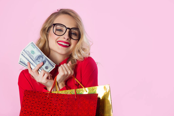 beautiful young girl in a red shirt with dollars and packages in their hands on a pink background - Photo, image