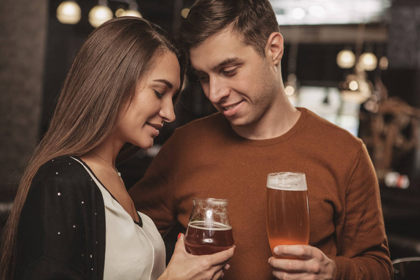Beautiful affectionate couple cuddling, while having drinks together at the bar. Handsome man embracinghis beautiful girlfriend, celebrating anniversary at the restaurant. Love, romance, valentines day concept - Photo, Image