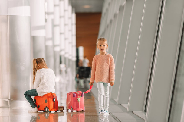 Güzel küçük kızlar havaalanında eğleniyor. Bavulun üzerinde oturmuş binmeyi bekliyorlar. - Fotoğraf, Görsel