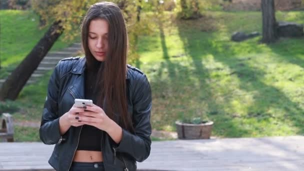 Closeup Of Beautiful Young Woman Playing With Her Hair. the girl goes in leather pants. The pretty young girl with natural make-up and sorting her long moving in wind hair while looking in camera - Filmagem, Vídeo