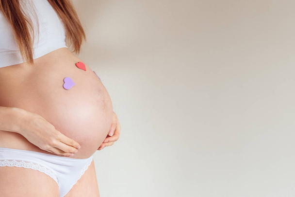 Живот беременной женщины 7 месяцев крупным планом с приклеенными сердцами
 - Фото, изображение