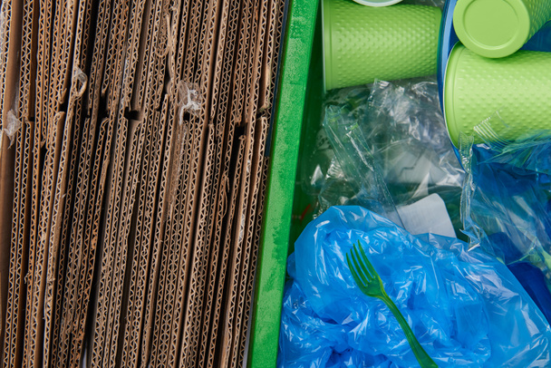 вид сверху на мусор с картонными, скомканными пластиковыми пакетами, пластиковыми чашками и вилками
 - Фото, изображение