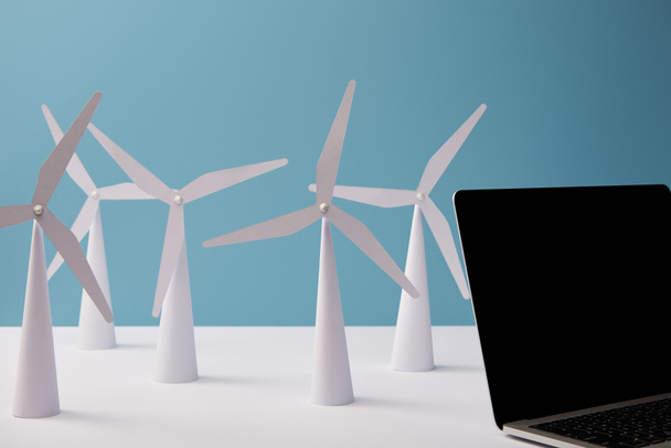 laptop na mesa branca com modelos de moinho de vento no fundo azul
 - Foto, Imagem
