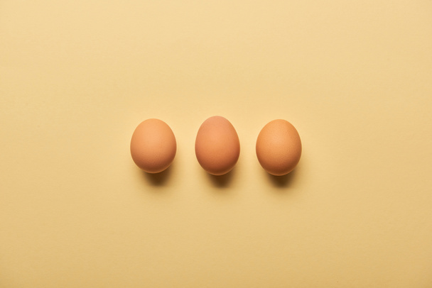 flat lay with brown organic eggs arranged in row on yellow background - Zdjęcie, obraz