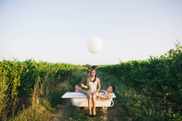 a man and a woman are sitting in a bath with rose petals in the middle of the vineyards - Photo, image