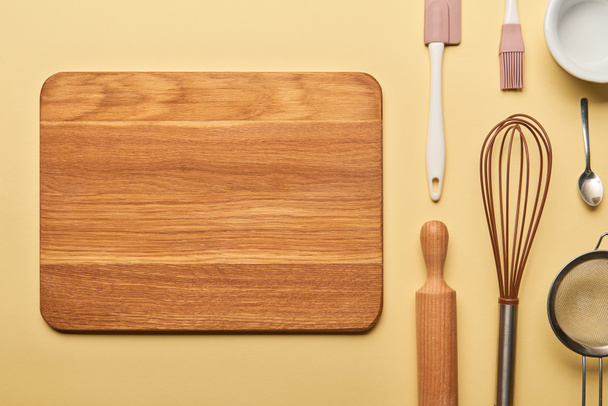 top view of empty wooden chopping board and cooking utensils on yellow background  - 写真・画像