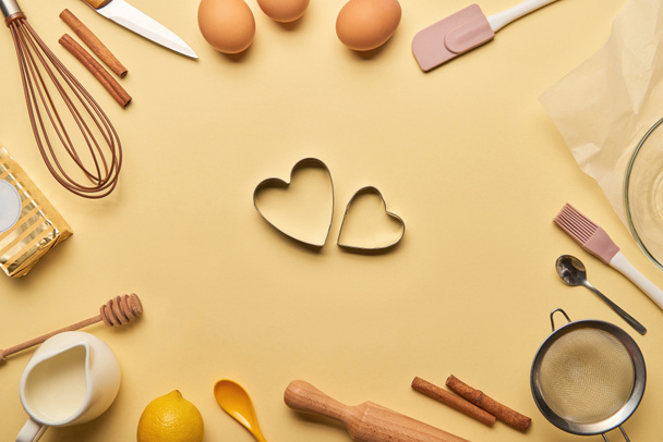 bovenaanzicht van bakkerij-ingrediënten en kookgerei rond hart gevormde deeg mallen - Foto, afbeelding