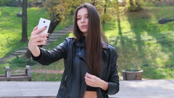 Closeup Of Beautiful Young Woman Playing With Her Hair. the girl goes in leather pants. The pretty young girl with natural make-up and sorting her long moving in wind hair while looking in camera - Záběry, video