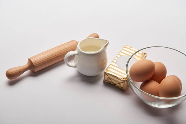 rolling pin, jar with milk, butter and eggs in bowl on grey background - Fotoğraf, Görsel