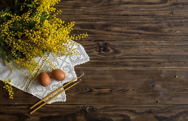 La composición de Pascua. Huevos, un ramo de mimosa amarilla y velas de iglesia en la mesa de madera de cerca. - Foto, Imagen