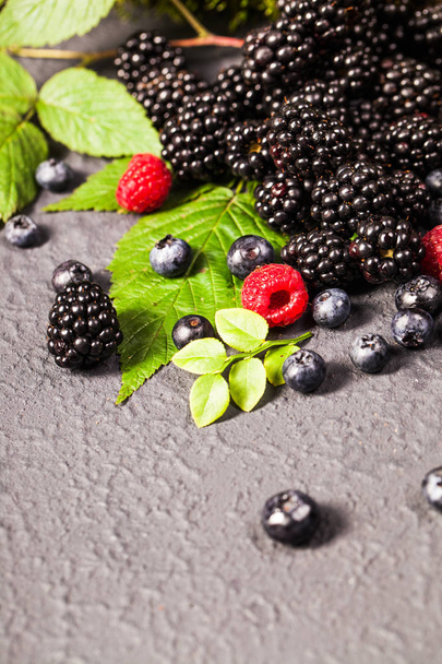 Freshly assorted berries in wooden bowl. Juicy and fresh blueberries6 blackberries and raspberries with green leaves on rustic background. Concept for healthy eating and nutritio - Photo, Image