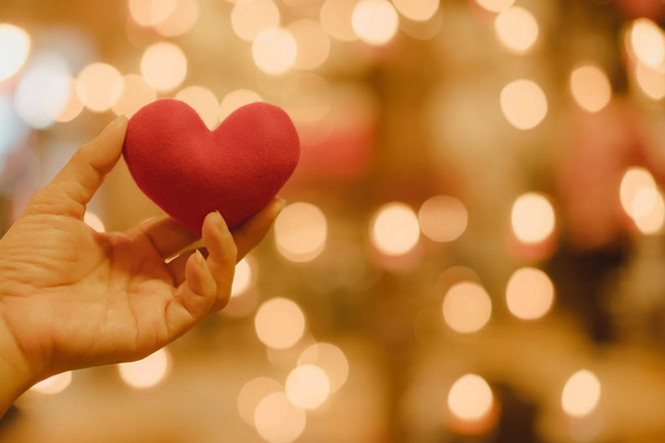 Ruce drží červené srdce tvaru polštář s krásným bokeh ve světle svíček. Pojem lásky v Valentine den. - Fotografie, Obrázek