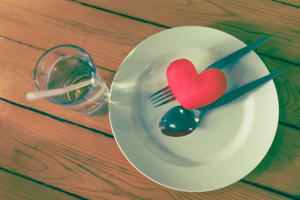 Pieni sydäntyyny lautasella haarukalla ja lusikka pöydällä
 - Valokuva, kuva