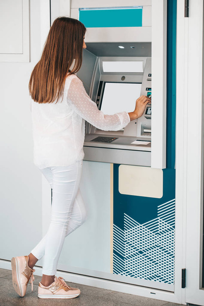 junge Frau hebt am Geldautomaten Geld von Kreditkarte ab - Bild - Foto, Bild