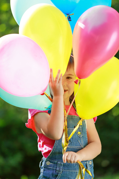 Little happy girl holding colorful balloons in green park - Photo, Image