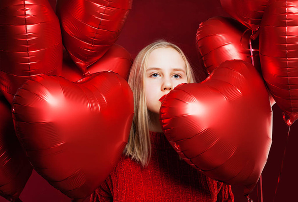 Νεαρή ξανθιά κοπέλα με την κόκκινη μπαλόνια καρδιά σε κόκκινο φόντο - Φωτογραφία, εικόνα